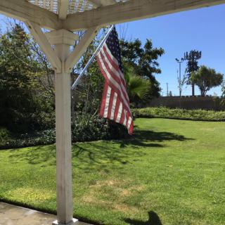 A sunny day view from a patio, featuring an American flag and a well-maintained garden.