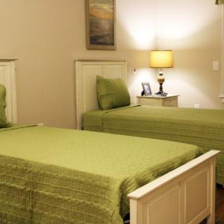 A cozy bedroom with twin beds featuring green bedding, accompanied by a nightstand and lamp.