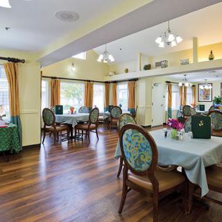 A well-lit dining area with elegant tables and chairs arranged on a wooden floor, complemented by large windows and tasteful decor.