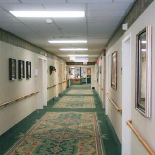 A long hallway with carpet and several doorways on either side, illuminated by overhead lighting.