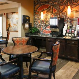 A cozy hotel lobby featuring a coffee station and seating area with modern furnishings and artistic wall decor.