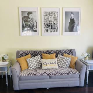 A modern living room with a stylish grey sofa, adorned with patterned and yellow accent pillows, and three framed artworks on the wall.