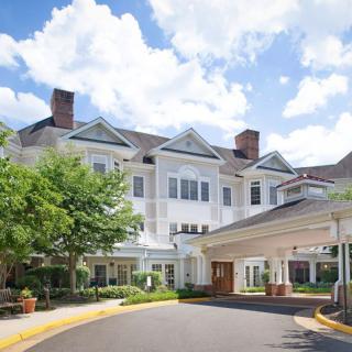 A large residential building with a driveway and landscaped greenery under a partly cloudy sky.