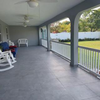 A spacious covered porch with rocking chairs overlooks a green lawn.