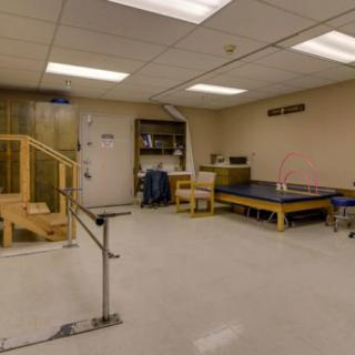 A spacious physical therapy room equipped with parallel bars, a staircase, and a treatment table for rehabilitation exercises.