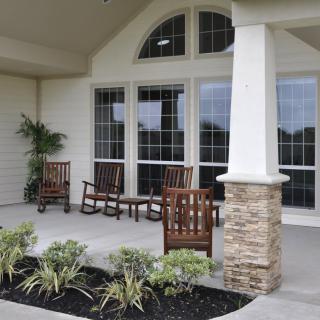 A cozy porch with wooden chairs and potted plants, featuring large windows and stone accents.