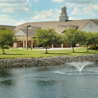 A scenic view of a building with a fountain in the pond and trees surrounding it.