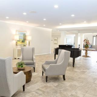 A spacious modern living room featuring a grand piano, elegant armchairs, and minimalist decor with soft lighting.