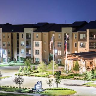A well-lit modern apartment complex at night with landscaped surroundings.