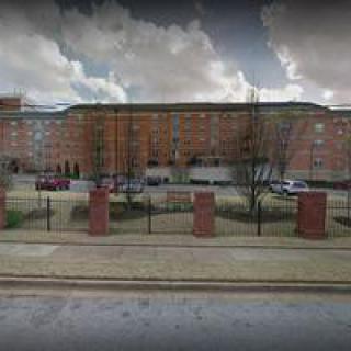 A brick residential building with a fence in front, set against a cloudy sky.