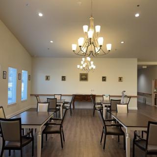 A spacious dining room with elegant chandeliers and neatly arranged tables and chairs.