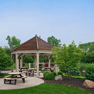 A peaceful park scene featuring a gazebo and picnic tables surrounded by lush greenery.