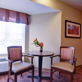 A cozy corner featuring a small table with two chairs, adorned with a vase of flowers and a painting on the wall.
