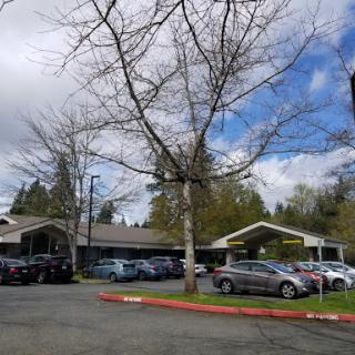 A view of a building with a parking lot surrounded by trees under a partly cloudy sky.