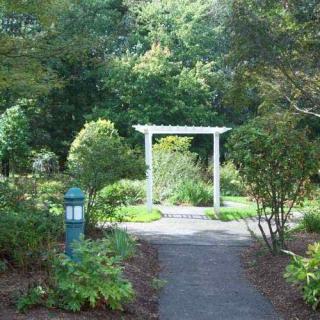 A scenic garden path leading to a white archway surrounded by lush greenery.