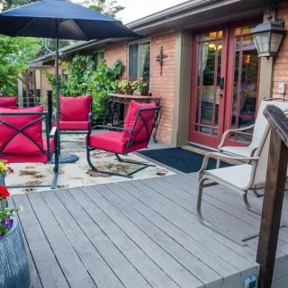 A cozy patio with red cushioned chairs, an umbrella, and surrounding greenery on a wooden deck.