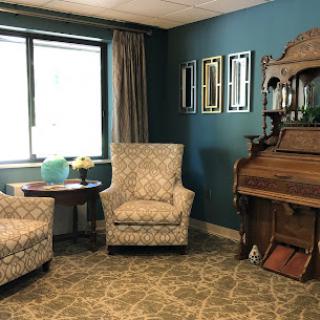 A cozy living room featuring patterned chairs, a vintage piano, and tasteful wall decorations.