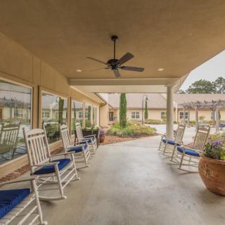 A cozy patio area with rocking chairs and a ceiling fan, offering a relaxing garden view.