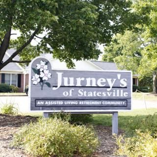 Sign for Jurney's of Statesville, an assisted living community, surrounded by trees and a building.