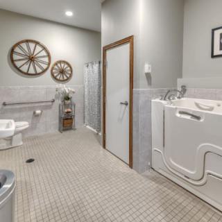 A spacious, accessible bathroom featuring a walk-in tub, toilet, and shower with grab bars for safety.