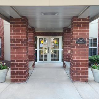 Entrance with brick columns and glass doors flanked by potted plants.