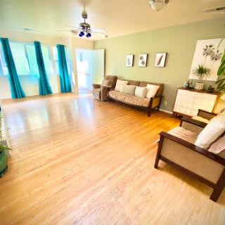 A spacious and well-lit living room featuring a wood floor, comfortable seating, and colorful accents.