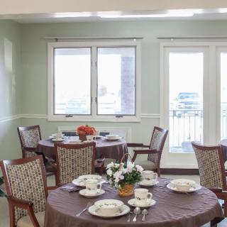 A cozy dining room with elegantly set tables and comfortable chairs, featuring floral centerpieces and a bright atmosphere.