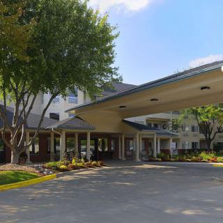 The entrance of a building with a covered driveway surrounded by trees on a clear day.