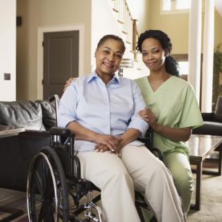 A caregiver smiling with an elderly person in a wheelchair.