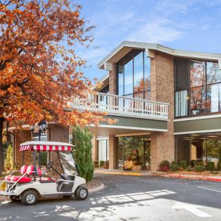 A golf cart parked outside a modern building surrounded by autumn trees.