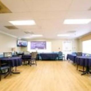 A cozy dining area with round tables and chairs, a television on the wall, and a wooden floor.