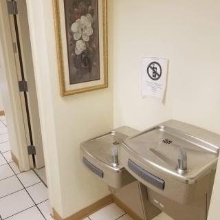 Two water fountains in a hallway with a framed artwork and a sign on the wall.