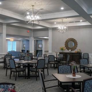 An elegantly decorated dining area featuring numerous tables and chairs, with chandeliers and a carpeted floor.