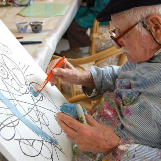 An elderly artist focused on painting a canvas with intricate designs.
