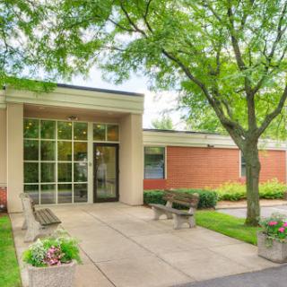 A welcoming entrance to a modern building surrounded by green trees and blooming flowers.