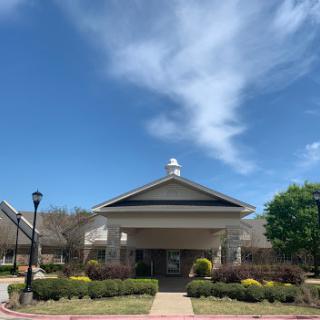 A peaceful view of a welcoming building framed by vibrant greenery and a blue sky.