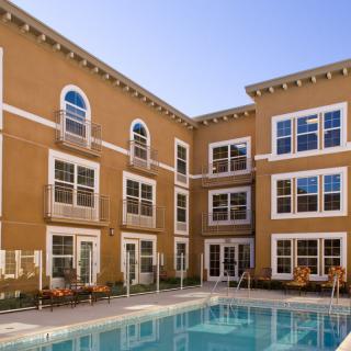 An exterior view of an apartment complex with a swimming pool in the foreground.
