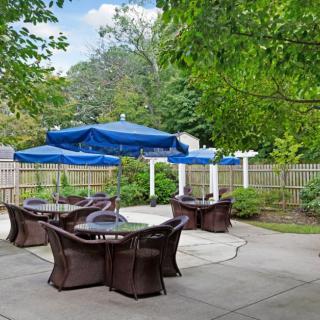 A tranquil outdoor patio with blue umbrellas and wicker furniture surrounded by greenery.