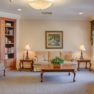A cozy living room with a comfortable sofa, classic lamps, and a wooden coffee table, framed by bookshelves and artwork.