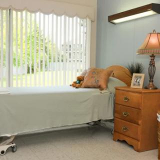 A neatly arranged bedroom with a single bed, nightstand, and a lamp by the window.