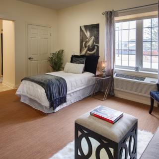 A cozy bedroom with a single bed, decorated with modern furnishings and a large window.