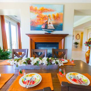 A vibrant dining room with an elegantly set table, featuring colorful plates and a centerpiece of flowers. A painting hangs above the fireplace, adding warmth to the room.