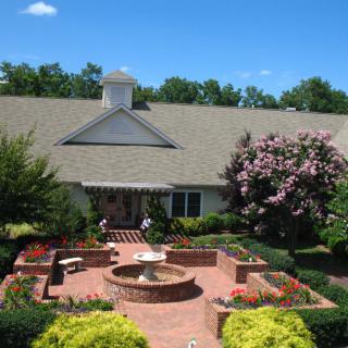A beautiful house with a well-maintained garden featuring a central fountain, surrounded by vibrant flowers and lush greenery.