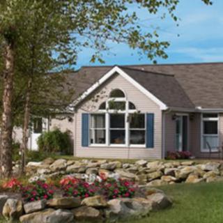 A single-story house with a well-maintained garden and blue shutters, surrounded by rocks and flowers.