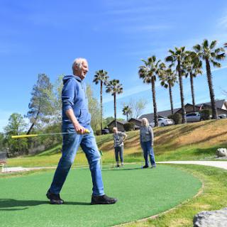 A sunny day at a mini golf course, with two people enjoying the game amidst palm trees.