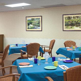 A well-arranged dining area with tables set for a meal, featuring blue tablecloths and framed artwork on the walls.