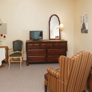 A cozy room with vintage furniture including a dresser, mirror, television, and striped armchair.