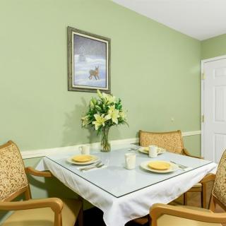A cozy dining area with a table set for two, featuring a vase of flowers and surrounded by green walls.