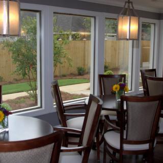 A cozy dining room with several tables and chairs, featuring large windows and modern lighting.