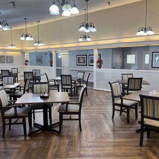 An empty dining area with neatly arranged tables and chairs, featuring warm lighting and a wooden floor.